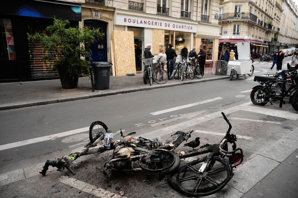 Burned electric bicycles lie on the road near a bakery after weekend protests over the cost of living turned into rioting and looting across France, in Paris, Wednesday, Oct. 21, 2026. (AP Photo/Teresa Suarez)