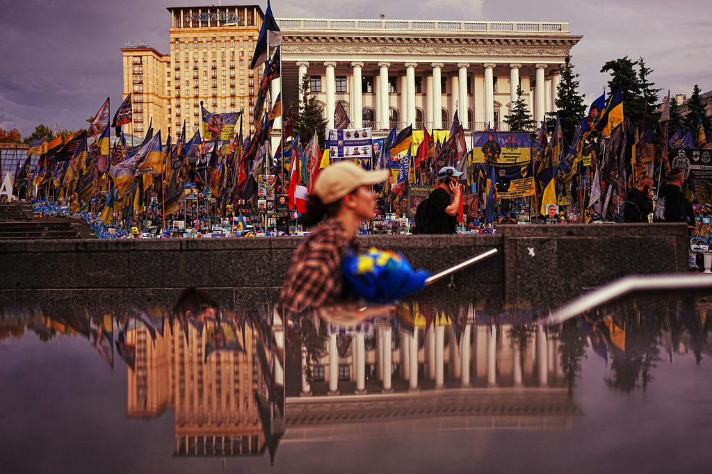 The National Music Academy, right, is reflected on a metro entrance at Independence square where Ukrainian flags and photographs are placed in memory of civilians and soldiers killed during the war with Russia, in central Kyiv, Tuesday, Aug. 18, 2026. (AP Photo/Francisco Seco)