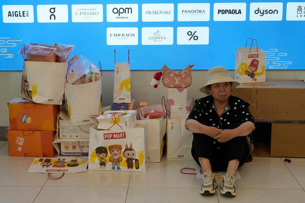A woman rests near bags of Labubu merchandise from PopMart at a mall, in Beijing, Friday, June 13, 2025. (AP Photo/Ng Han Guan)