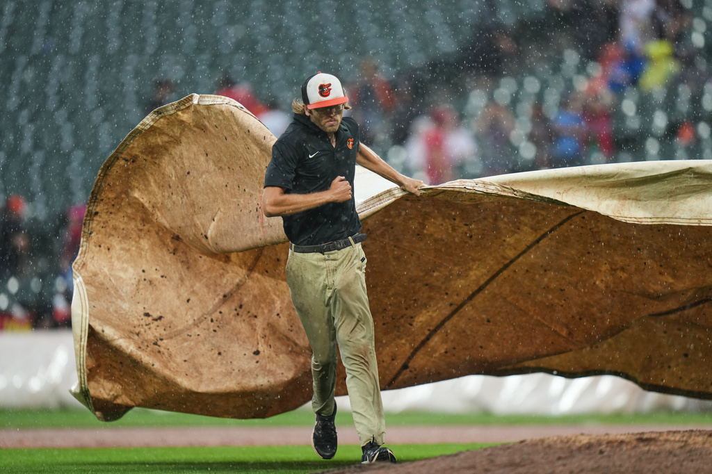 A member of the grounds crew places a tarp over the mound as a baseball game between the Baltimore Orioles and the Philadelphia Phillies is delayed for the second time due to rain, Sunday, Aug. 2, 2026, in Baltimore. (AP Photo/Stephanie Scarbrough)