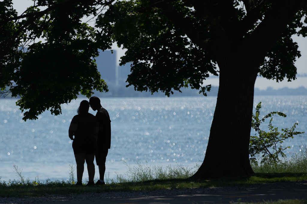 A couple stand in the shade near the Detroit River to avoid the heat Monday, July 13, 2026, in Detroit. (AP Photo/Paul Sancya)