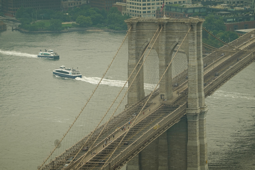 Boats maneuver the East River near the Brooklyn Bridge as smoke from wildfires blankets the sky Thursday, July 16, 2026, in New York. (AP Photo/Alyssa Goodman)