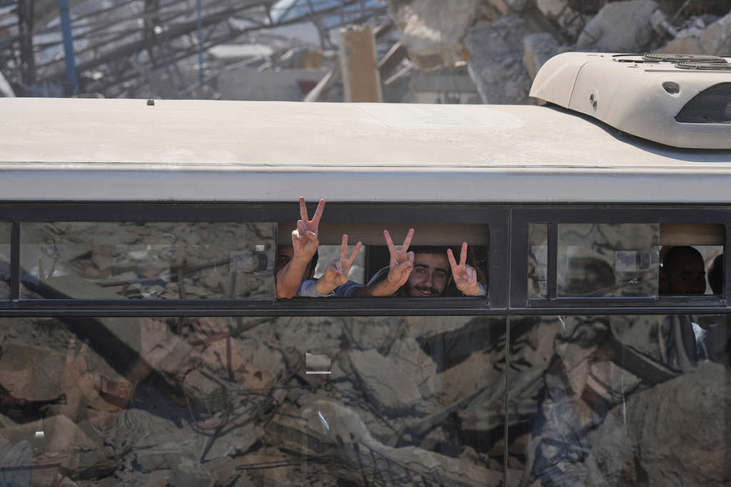 Freed Palestinian prisoners on a bus flash the victory sign as they pass destroyed buildings in the Gaza Strip after their release from Israeli jails under a ceasefire agreement between Hamas and Israel, in Khan Younis, southern Gaza Strip, Monday, Oct. 13, 2025. (AP Photo/Jehad Alshrafi)