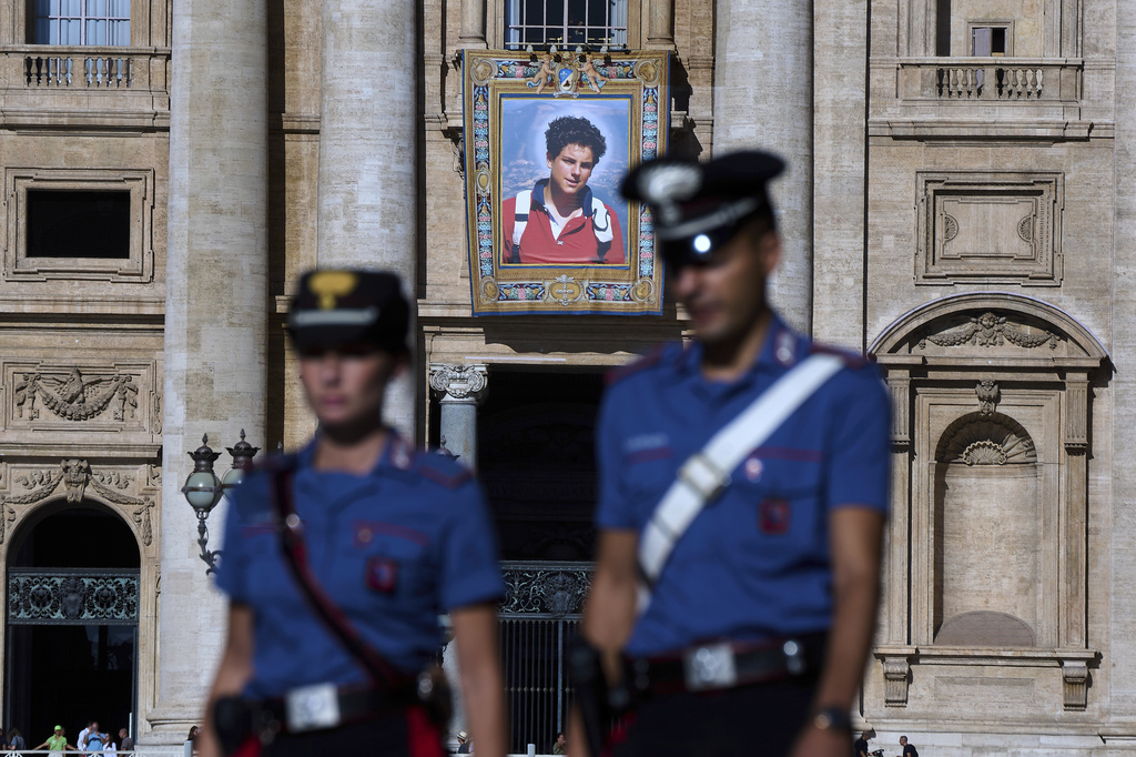 A tapestry with a portrait of Blessed Carlo Acutis, who will be canonized on Sunday, hangs on the facade of St. Peter's Basilica at the Vatican, Thursday, Sept. 4, 2025, as two Carabinieri officers patrol in St. Peter's Square. (AP Photo/Domenico Stinellis)
