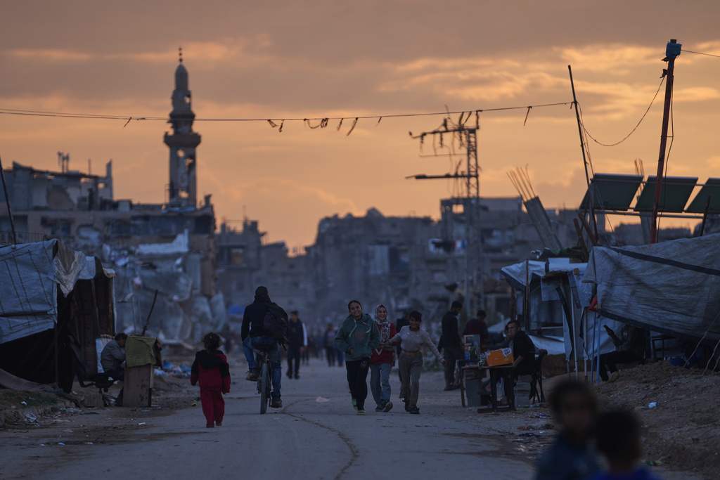Palestinian youth walk along a tent camp for displaced people as the sun sets in Nuseirat, central Gaza Strip, Friday, Dec. 26, 2025. (AP Photo/Abdel Kareem Hana)