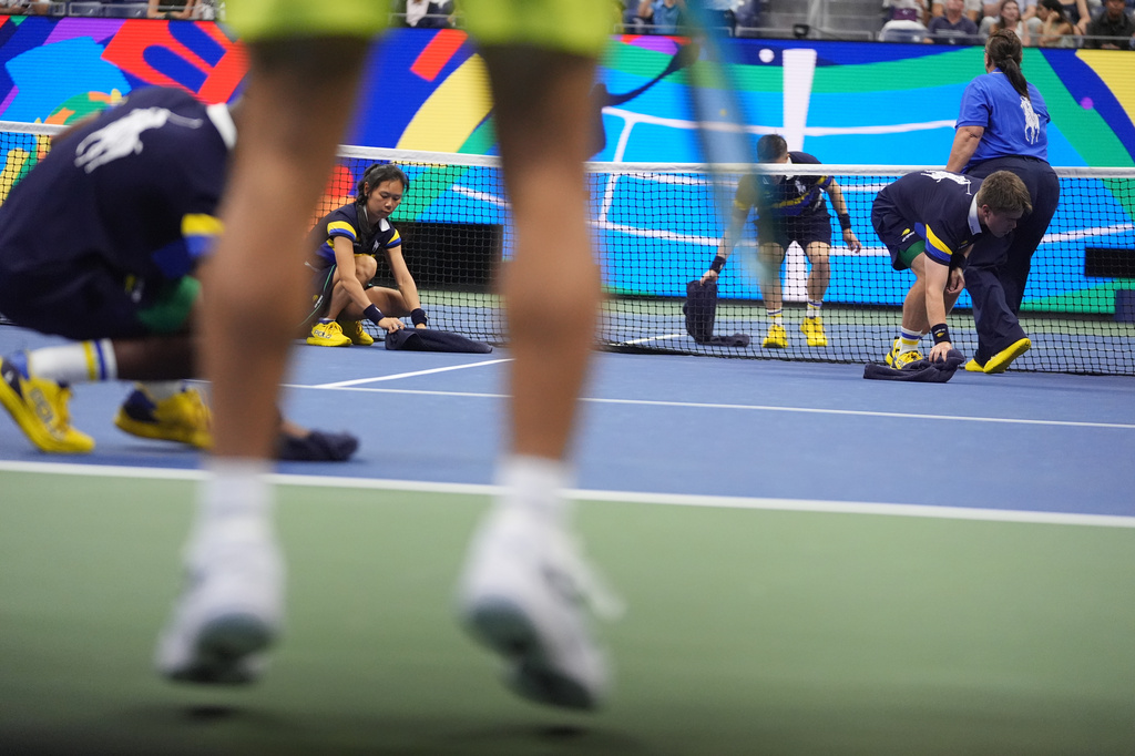 Ball persons wipe the floor during a break in play between Novak Djokovic, of Serbia, and Mariano Navone, of Argentina, during the first round of the U.S. Open tennis championships Sunday, Aug. 30, 2026, in New York. (AP Photo/Frank Franklin II)