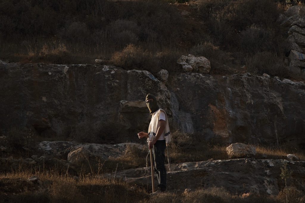 An Israeli settler stands on a hill as Israeli soldiers block access for Palestinians to an area for harvesting olives in the West Bank village of Sa'ir, near Hebron, Thursday, Oct. 23, 2025. (AP Photo/Leo Correa)