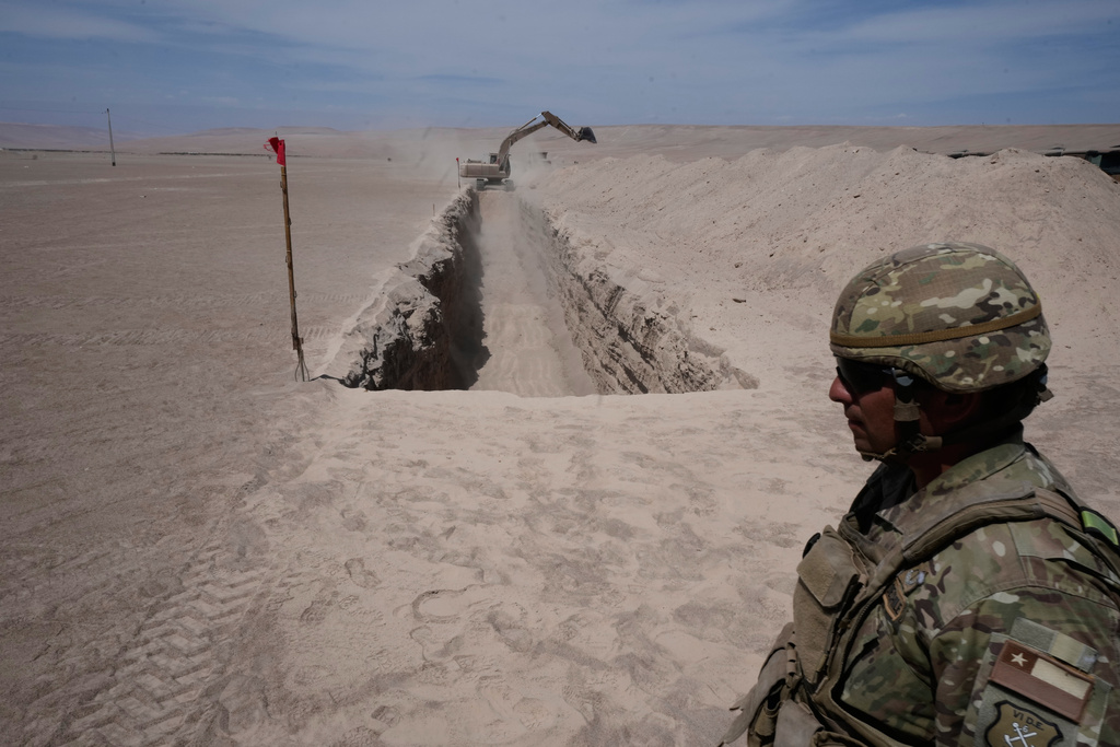 A soldier stands near a machine digging along the northern border at the Chacalluta border crossing, in Arica, Chile, Monday, March 16, 2026, as part of the measures to deter irregular migration. (AP Photo/Esteban Felix)