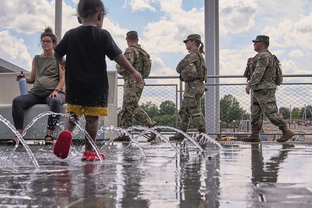 Armed members of the Ohio National Guard pass by children playing in a water feature at The Wharf, Monday, Aug. 25, 2025, in Washington. (AP Photo/Jacquelyn Martin)