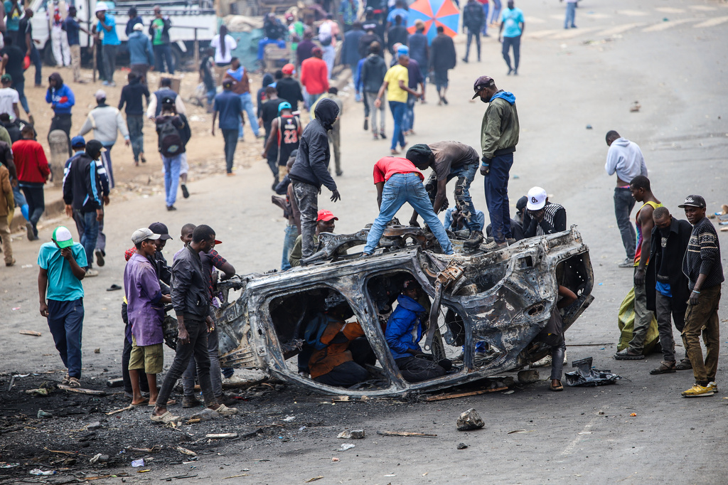 People strip parts from a burned-out vehicle during a public transport strike over fuel prices in Nairobi, Kenya, Monday, May 18, 2026. (AP Photo/Patrick Ngugi)
