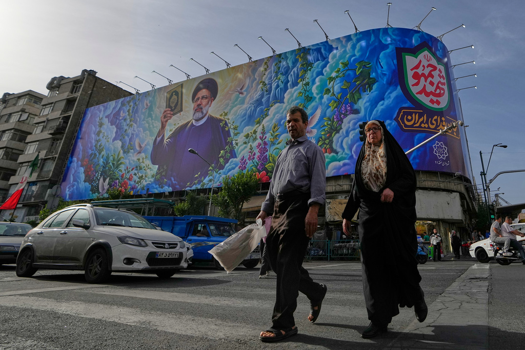 People cross an intersection in front of a billboard showing a portrait of the late Iranian President Ebrahim Raisi, who was killed in a helicopter crash in 2024, in downtown Tehran, Iran, Thursday, May 28, 2026. (AP Photo/Vahid Salemi)
