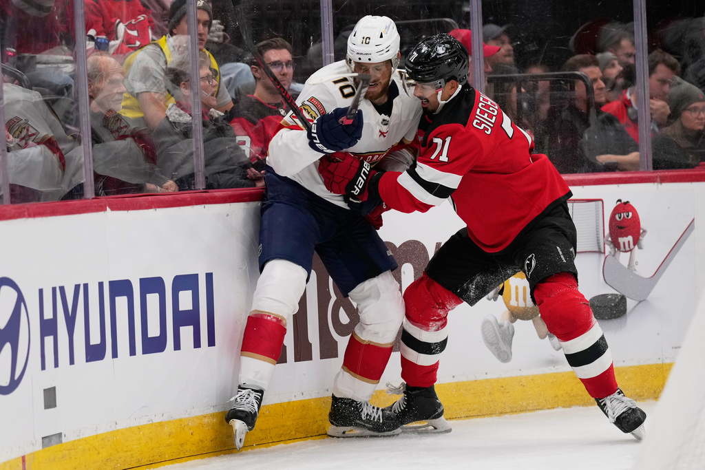 New Jersey Devils' Jonas Siegenthaler, right, hits Florida Panthers' A.J. Greer up against the boards during the first period of an NHL hockey game Thursday, Oct. 16, 2025, in Newark, N.J. (AP Photo/Seth Wenig)