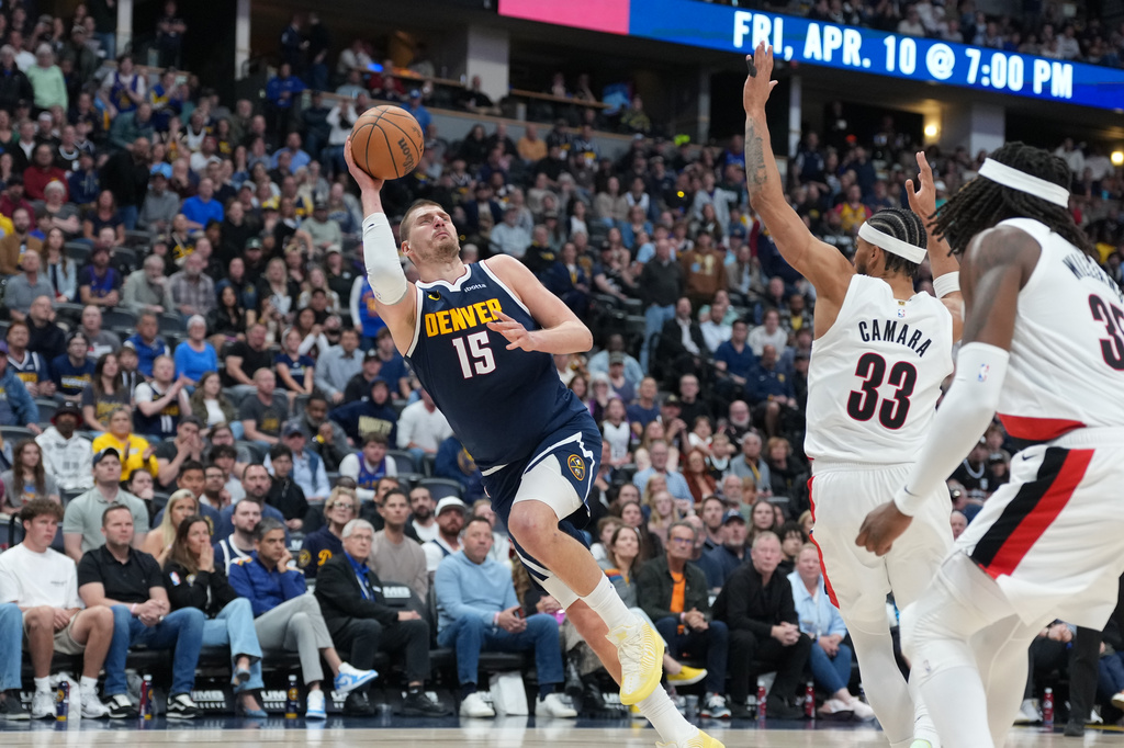Denver Nuggets center Nikola Jokić, left, falls as he puts up a shot after being fouled by Portland Trail Blazers forward Toumani Camara, back right, as center Robert Williams III looks on in the second half of an NBA basketball game Monday, April 6, 2026, in Denver. (AP Photo/David Zalubowski)