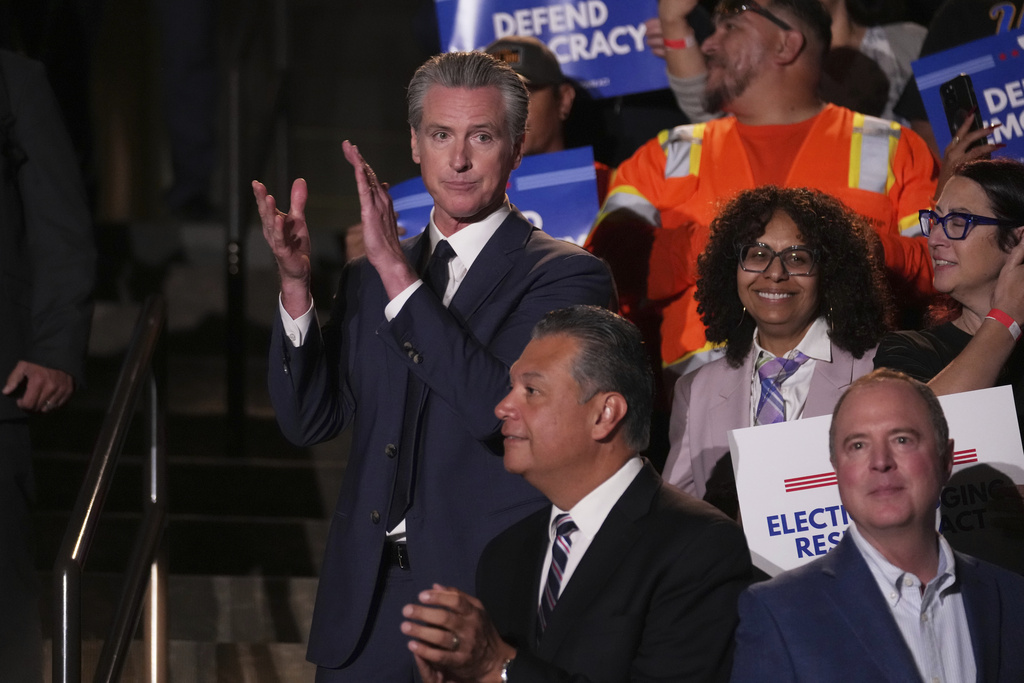 California Gov. Gavin Newsom, left, applauds as he stands above Sen. Adam Schiff, D-Calif., below right, and Sen. Alex Padilla, D-Calif., below center, during a news conference Thursday, Aug. 14, 2025, in Los Angeles. (AP Photo/Marcio Jose Sanchez)