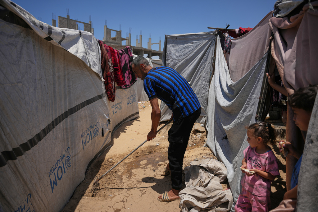 Khaled Kollab cleans a drainage pit in front of his family's tent in Khan Yunis, southern Gaza Strip, Wednesday, June 3, 2026. (AP Photo/Abdel Karim Hanna)