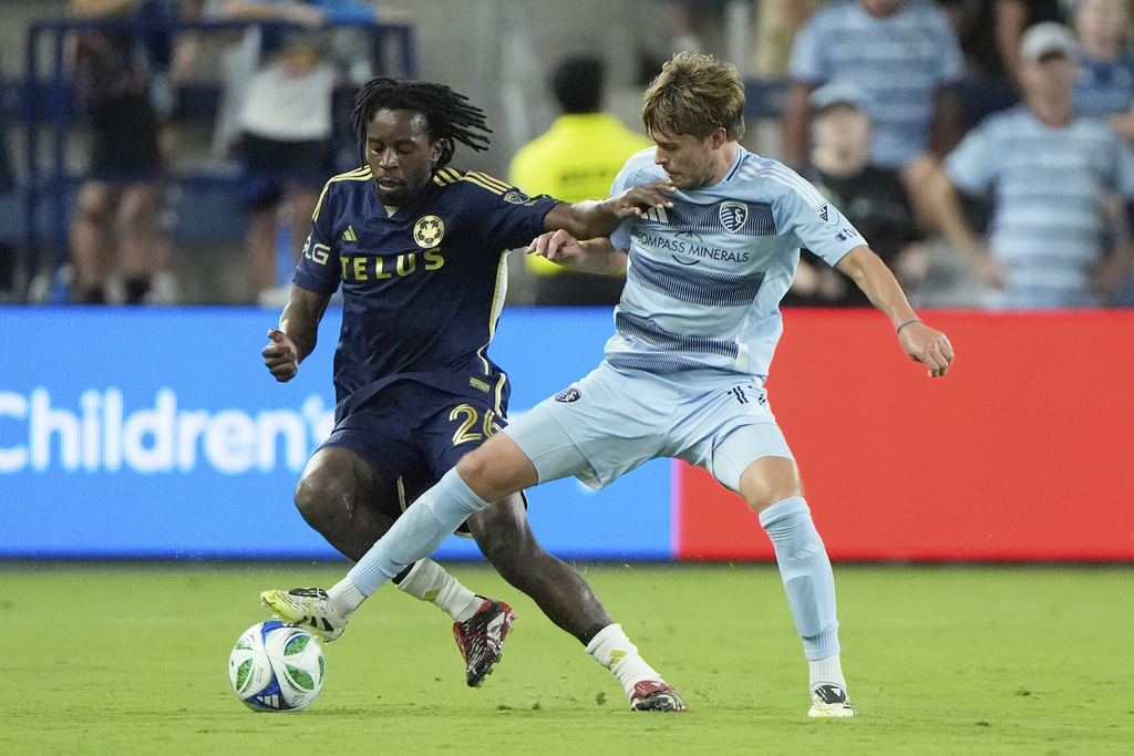 Sporting Kansas City midfielder Jake Davis, right, kicks the ball under pressure from Vancouver Whitecaps midfielder Jean-Claude Ngando (26) during the second half of an MLS soccer match Saturday, Sept. 20, 2025, in Kansas City, Kan. (AP Photo/Charlie Riedel)