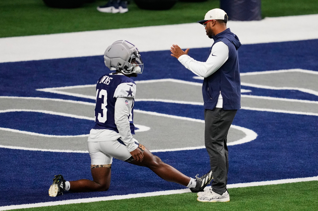 Dallas Cowboys safety Caleb Downs talks with defensive coordinator Christian Parker, right, as he stretches before an NFL football practice Wednesday, Aug. 26, 2026, in Frisco, Texas. (AP Photo/Tony Gutierrez)