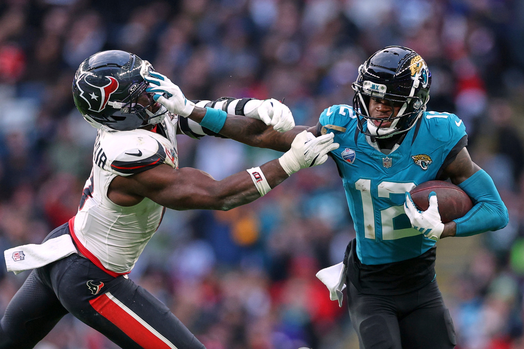 Jacksonville Jaguars wide receiver Travis Hunter (12) holds off Houston Texans linebacker Azeez al-Shaair (0) during an NFL football game in London, Sunday, Oct. 18, 2026. (AP Photo/Ian Walton)