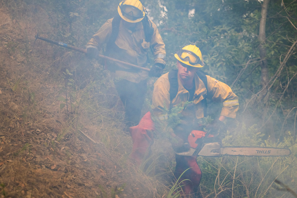 A firefighter cuts brush to stop the Timber Fire from burning above Deetjen's Inn in Big Sur, Calif., Tuesday, Aug. 11, 2026. (AP Photo/Nic Coury)