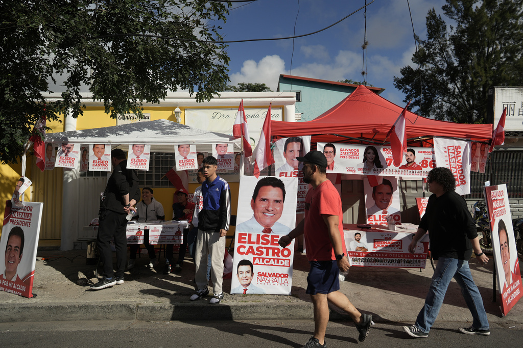 People walk past a candidate's stand with campaign materials during general elections in Tegucigalpa, Honduras, Sunday, Nov. 30, 2025. (AP Photo/Emmanuel Andres)
