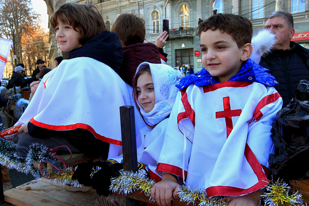 Georgian children take part in a religious procession to the Holy Trinity Cathedral to mark Orthodox Christmas in Tbilisi, Georgia, Wednesday, Jan. 7, 2026, with the building of Georgian Parliament on the left. (AP Photo/Shakh Aivazov)