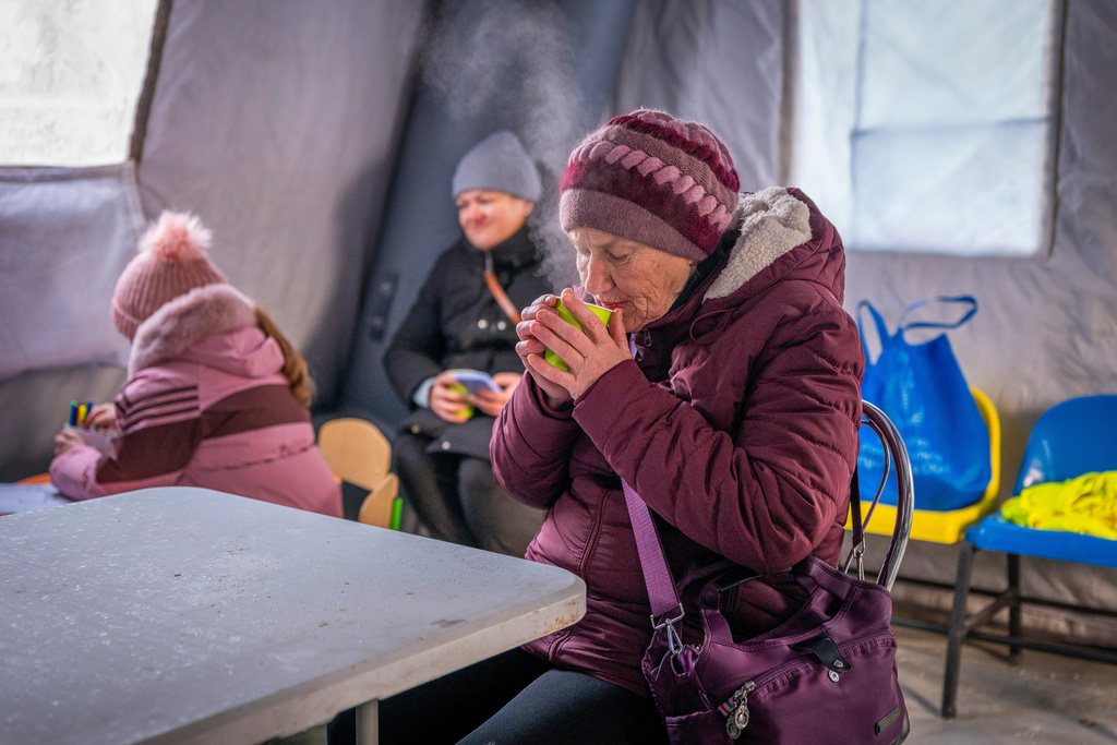 A woman gets warm with a hot cup of tea at an emergency center set up to support people during power outages caused by Russia's regular air attacks on the country's energy infrastructure, in Boryspil, Ukraine, Wednesday, Jan. 14, 2026. (AP Photo/Dan Bashakov)