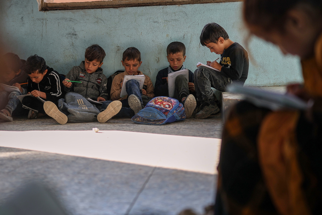 Students write in their notebooks while sitting on the floor inside a classroom of the Maar Shmarin Primary School, scarred by bullet holes dating back to the fighting between forces loyal to former President Bashar Assad and rebel groups, in the village of Maar Shmarin, in the Idlib countryside, Syria, Sunday, Oct. 19, 2025. (AP Photo/Ghaith Alsayed)