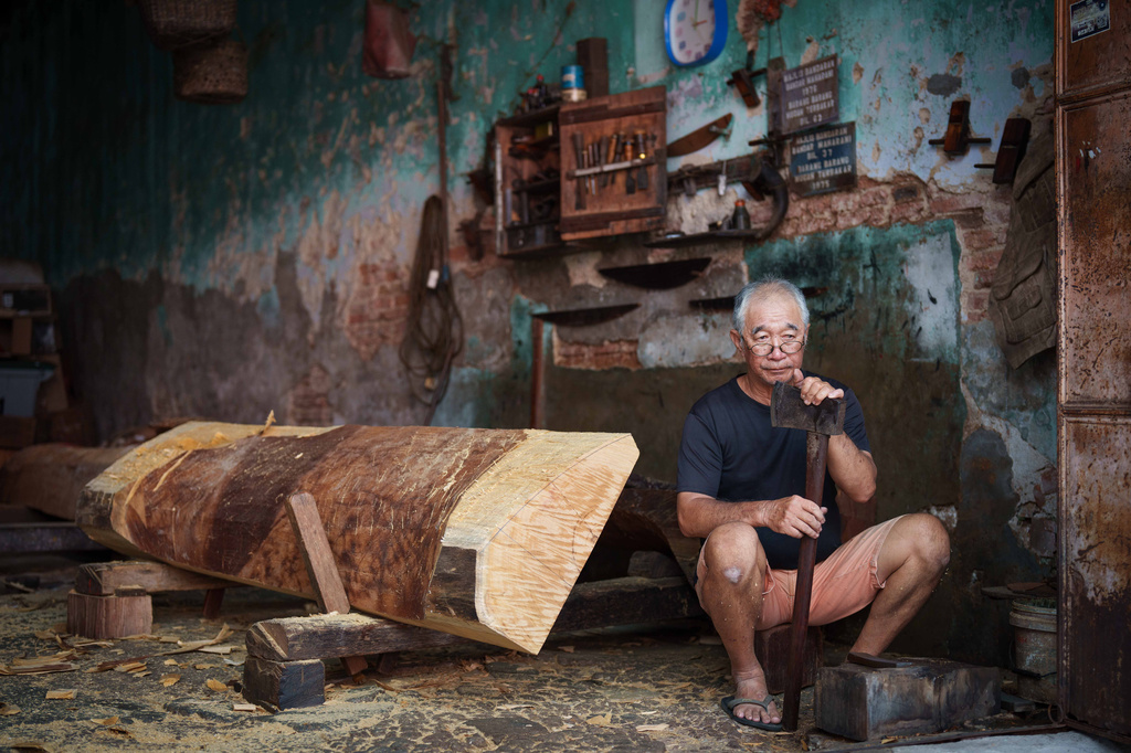 Goh Khuay Hou sits with an axe during the early stages of making a Mei Hua coffin at his family's workshop in Muar, Malaysia, Monday, Sept. 7, 2026. (AP Photo/Vincent Thian)