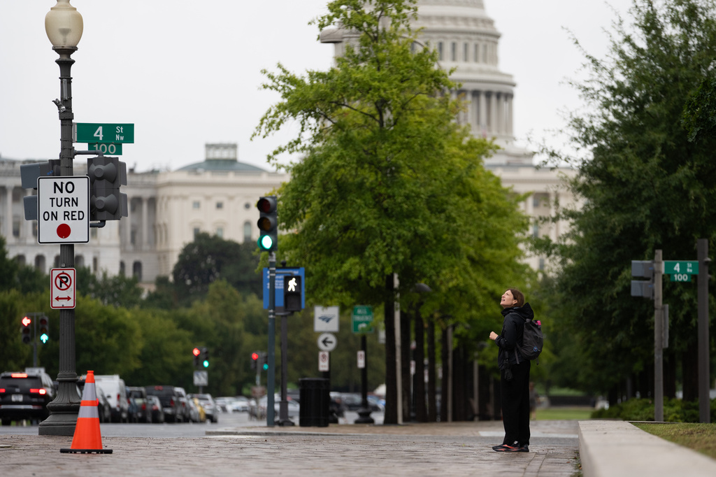 An individual watches a protester scale a light pole and unfurl a banner to protest the upcoming State Visit by China's President Xi Jinping, Tuesday, Sept. 22, 2026, in Washington. (AP Photo/Allison Robbert)