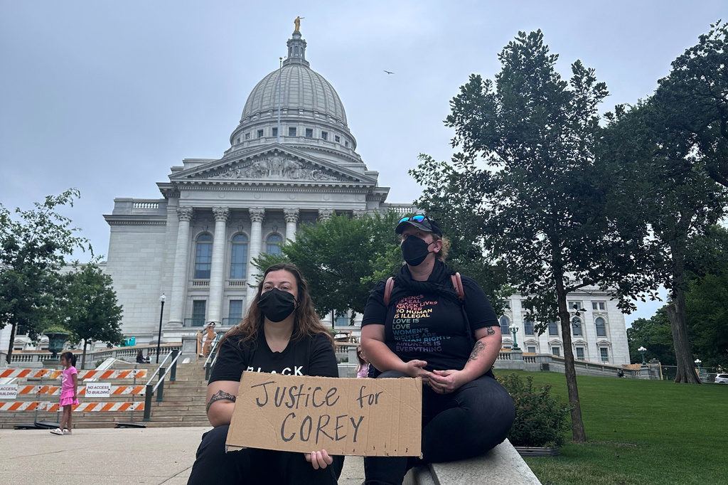Lilly Nimmer, left, and Reba Bergmann, right, hold a sign to protest the police shooting of Corey Ruiz outside of the Wisconsin state Capitol during the weekly farmers market on Saturday, July 25, 2026, in Madison, Wisconsin. (AP Photo/Scott Bauer)
