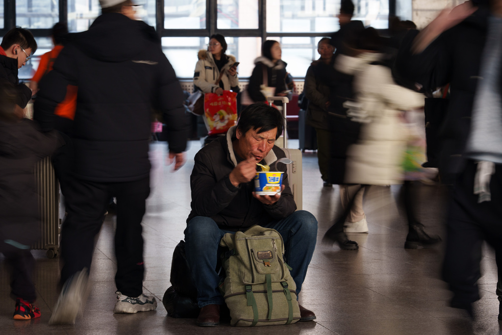 A traveler eats while waiting inside a railway station as people return home during the Lunar New Year holiday in Beijing, China, Tuesday, Feb. 10, 2026. (AP Photo/Vincent Thian)
