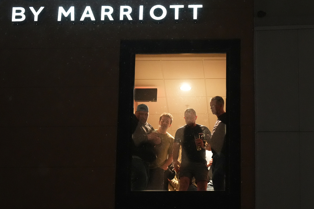 People inside a SpringHill Suites by Marriott hotel watch as law enforcement clash with protesters outside the hotel on Monday, Jan. 26, 2026, in Maple Grove, Minn. (AP Photo/Adam Gray)