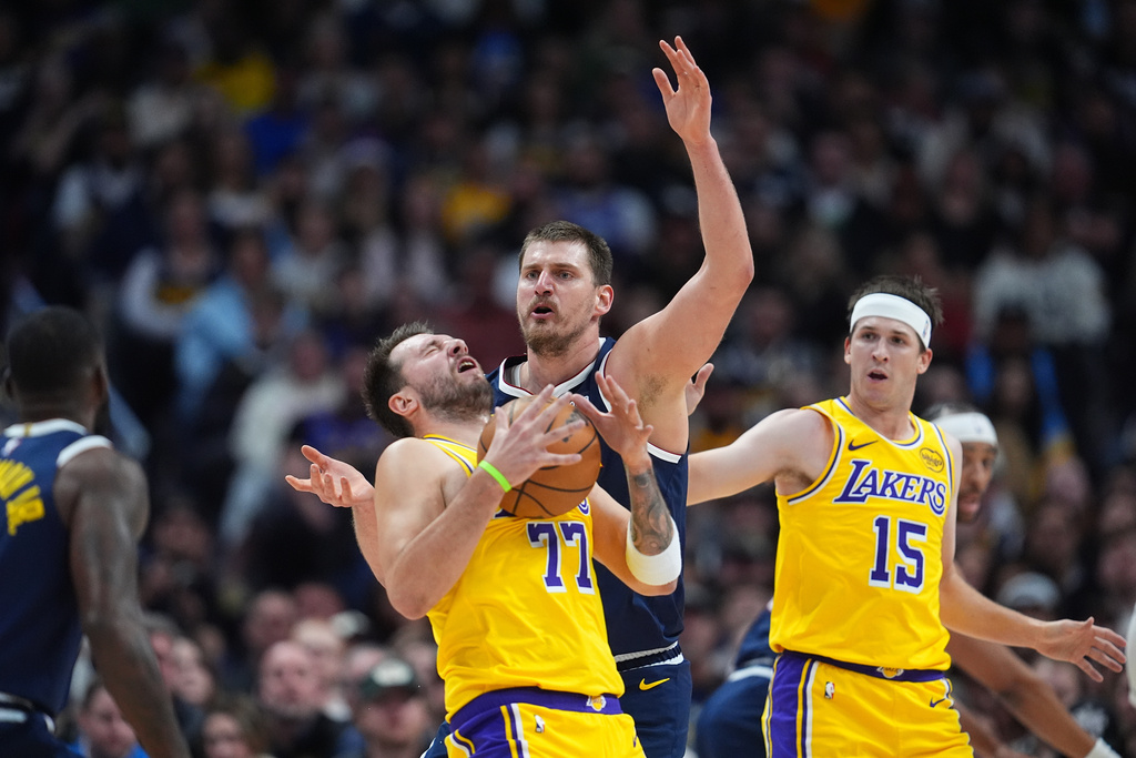 Los Angeles Lakers guard Luka Dončić, left, reacts after getting hit in the face by the ball while fighting for control with Denver Nuggets center Nikola Jokić as Los Angeles guard Austin Reaves, right, looks on in the first half of an NBA basketball game Thursday, March 5, 2026, in Denver. (AP Photo/David Zalubowski)