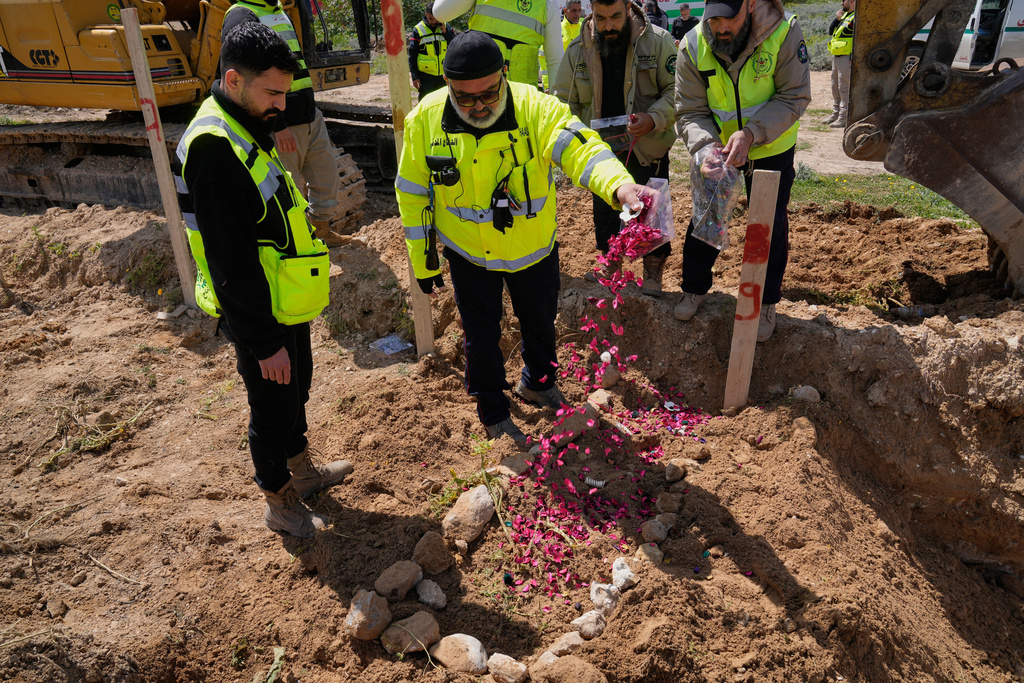 A paramedic scatters flower petals on the grave of his comrade who was killed in an Israeli airstrike, at a temporary mass grave in Tyre, south Lebanon, Wednesday, March 25, 2026. (AP Photo/Hussein Malla)