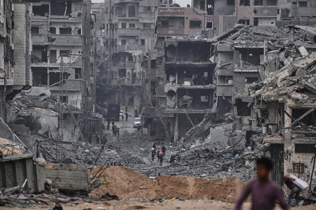 Palestinians walk past destroyed buildings in the Shati refugee camp in Gaza City, Sunday, Oct. 12, 2025, after Israel and Hamas agreed to a pause in their war and the release of the remaining hostages. (AP Photo/Abdel Kareem Hana)