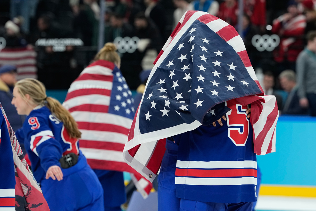 United States' Megan Keller (5), covered in the U.S. flag, gets a hug from a teammate after the United States' women's ice hockey team stand after being presented with the gold medals at the 2026 Winter Olympics, in Milan, Italy, Thursday, Feb. 19, 2026. (AP Photo/Petr David Josek)