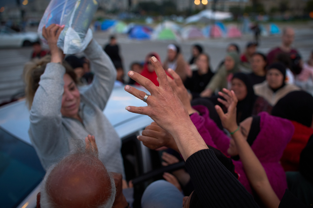 Displaced women reach out to receive an aid package distributed by a volunteer in Beirut, Lebanon, Friday, March 27, 2026. (AP Photo/Emilio Morenatti)