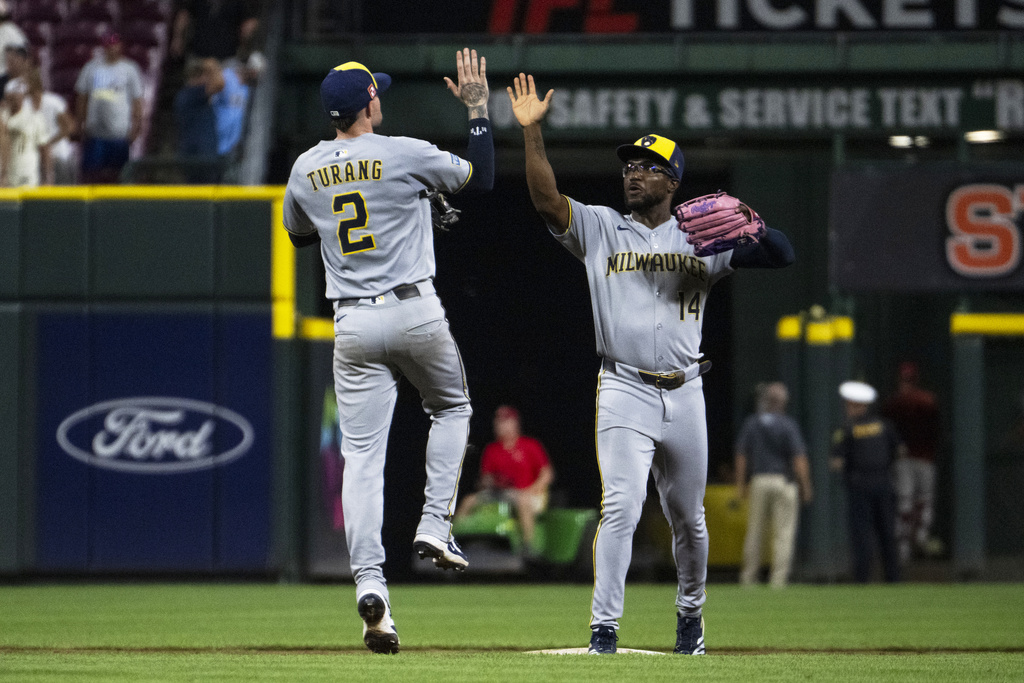 Milwaukee Brewers second base Brice Turang (2) and shortstop Andruw Monasterio (14) celebrate after beating the Cincinnati Reds in the 11th inning of a baseball game, Saturday, Aug. 16, 2025, in Cincinnati. (AP Photo/Michael Swensen)