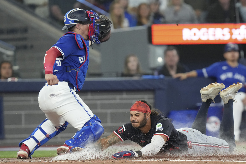 Minnesota Twins' Austin Martin (right) scores a run ahead of the tag from Toronto Blue Jays catcher Tyler Heineman (55) during fourth inning MLB baseball action in Toronto on Wednesday, August 27, 2025. (Chris Young/The Canadian Press via AP)
