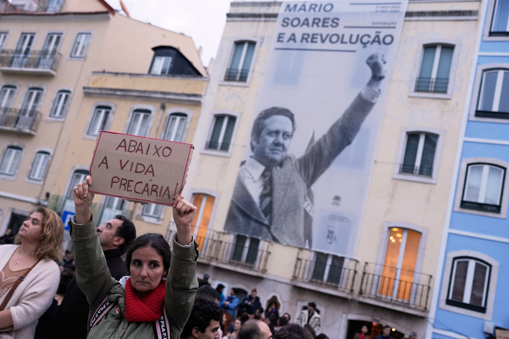 Demonstrators gather outside the parliament during a general strike to protest against a new labour package announced by the centre-right government, in Lisbon, Thursday, Dec. 11, 2025. The sign held by the woman reads in Portuguese: "Down with precarious living conditions." (AP Photo/Armando Franca)