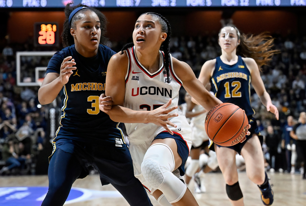 UConn guard Azzi Fudd, center, drives to the basket as Michigan guard Mila Holloway, left, defends in the first half of an NCAA college basketball game, Friday, Nov. 21, 2025, in Uncasville, Conn. (AP Photo/Jessica Hill)