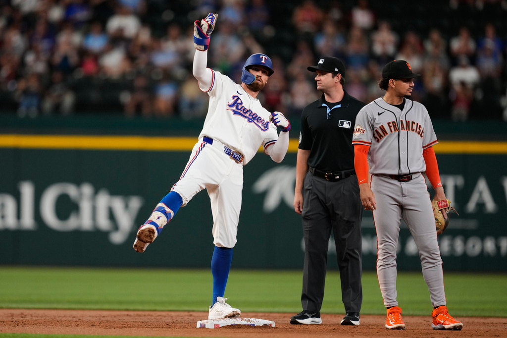 Texas Rangers' Brandon Nimmo, left, celebrates his run-scoring double in front of umpire Adam Beck and San Francisco Giants shortstop Willy Adames, right, in the first inning a baseball game in Arlington, Texas, Tuesday, Aug. 4, 2026. (AP Photo/Tony Gutierrez)