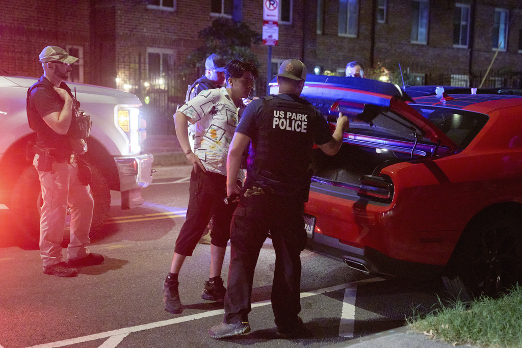 Agents from various agencies including Bureau of Alcohol, Tobacco, Firearms and Explosives, Park Police, and FBI, question a couple who had been parked outside a legal parking zone while eating McDonald's takeout, Tuesday, Aug. 12, 2025, in northwest Washington near Kennedy St. NW. The couple were released after a search of the car. (AP Photo/Jacquelyn Martin)
