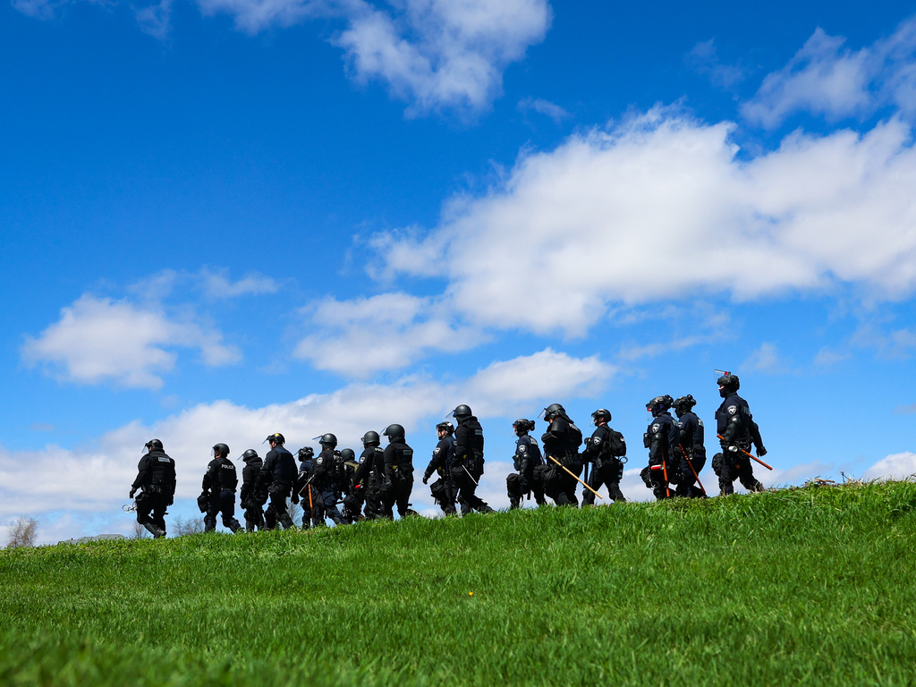 Law enforcement in riot gear walk in a field after animal welfare activists attempted to gain entry to Ridglan Farms beagle breeding and research facility on Saturday, April 18, 2026, in Blue Mounds, Wis. (Owen Ziliak/Wisconsin State Journal via AP)