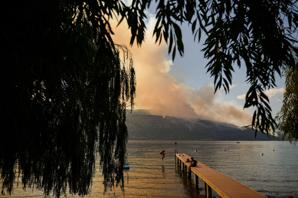FILE - A woman jumps off a dock into Okanagan Lake, in Lake Country, British Columbia, as the Quilpituk Creek wildfire burns on the mountainside across the lake near Fintry, Aug. 3, 2026. (Darryl Dyck/The Canadian Press via AP, File)