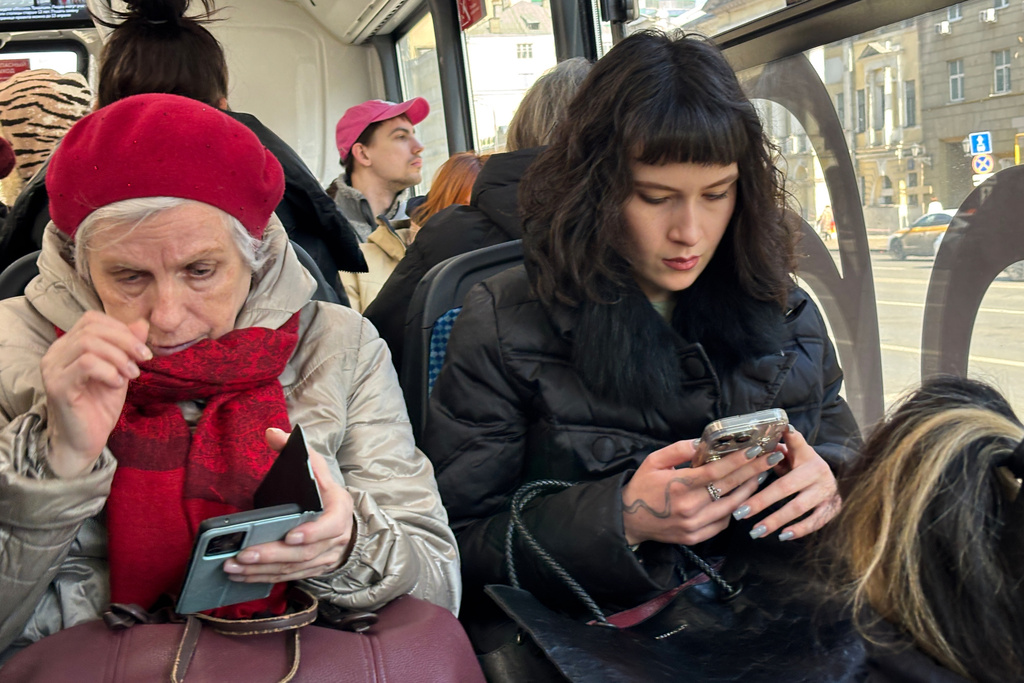 FILE - Women look at their smartphones while riding a bus in Moscow, on March 11, 2026. (AP Photo/Alexander Zemlianichenko, File)