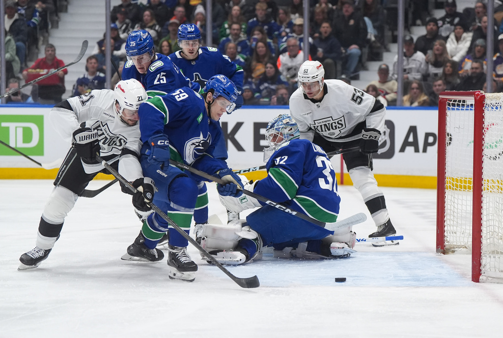 Vancouver Canucks' Kirill Kudryavtsev (59) and Los Angeles Kings' Scott Laughton (21) vie for the puck after Vancouver goalie Kevin Lankinen (32) made the save during the first period of an NHL hockey game, in Vancouver, on Tuesday, April 14, 2026. (Darryl Dyck/The Canadian Press via AP)