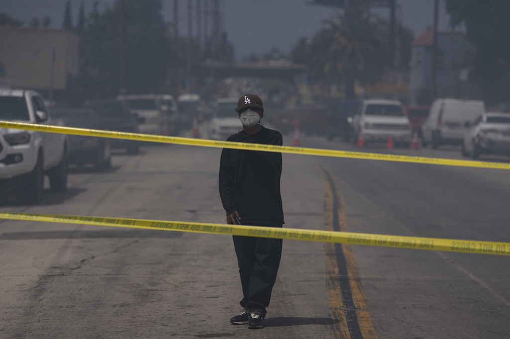 A person wears a mask while watching firefighters fight a warehouse fire in the Boyle Heights neighborhood of Los Angeles, Sunday, June 21, 2026. (AP Photo/Jae C. Hong)