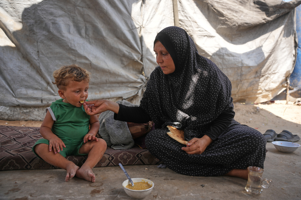 A Palestinian woman feeds a child a meal cooked using combustible materials collected from a garbage dump amid a shortage of cooking gas in Deir al-Balah, central Gaza Strip, Saturday, Aug. 22, 2026. (AP Photo/Abdel Kareem Hana)