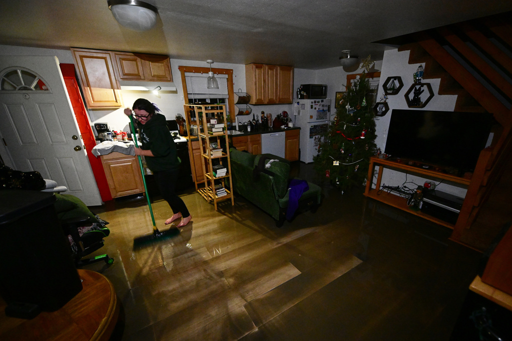 A resident sweeps water and mud in her house after flooding Wednesday, Dec. 24, 2025, in Wrightwood, Calif. (AP Photo/Wally Skalij)